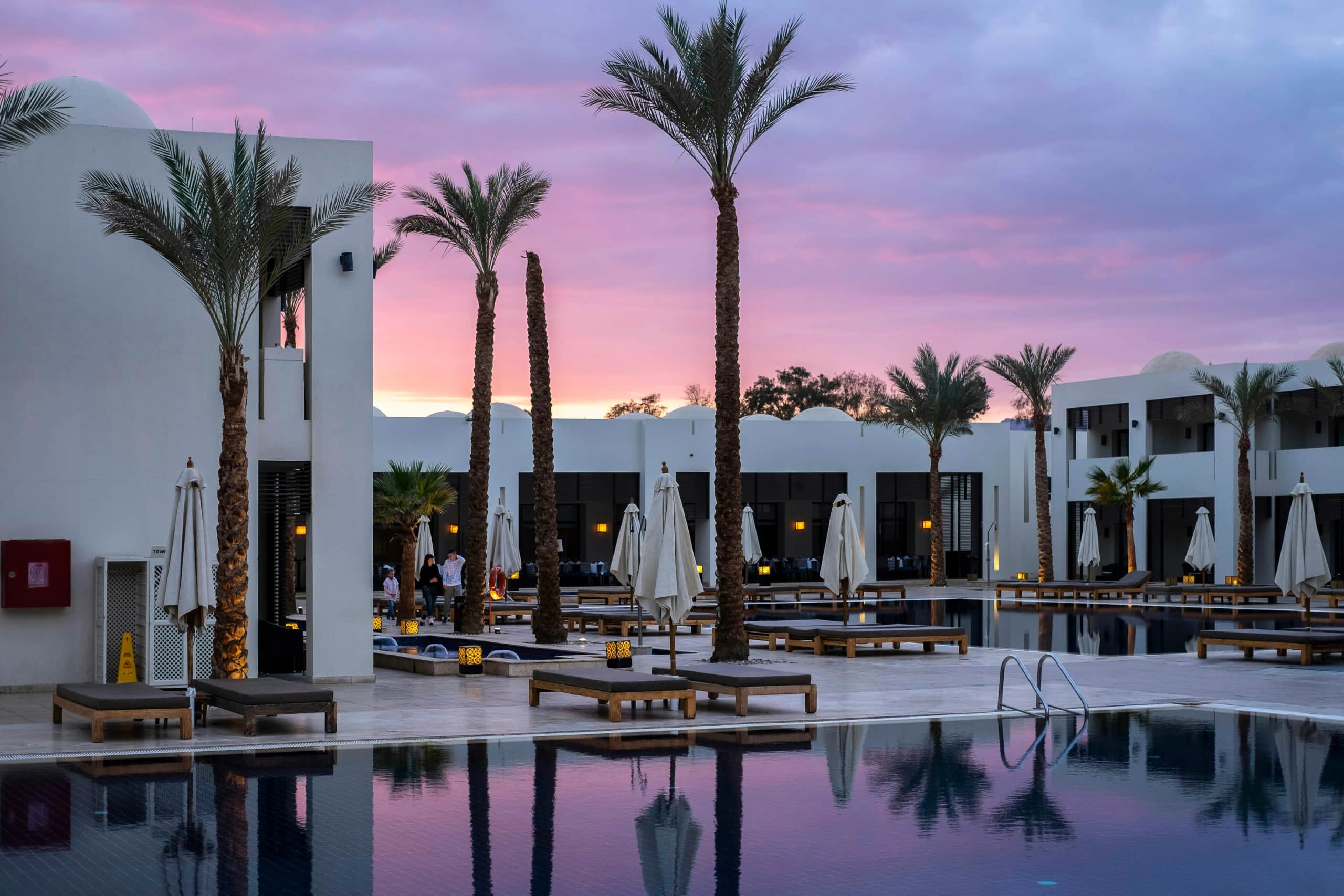 Resort swimming pool surrounded by palm trees at sunset